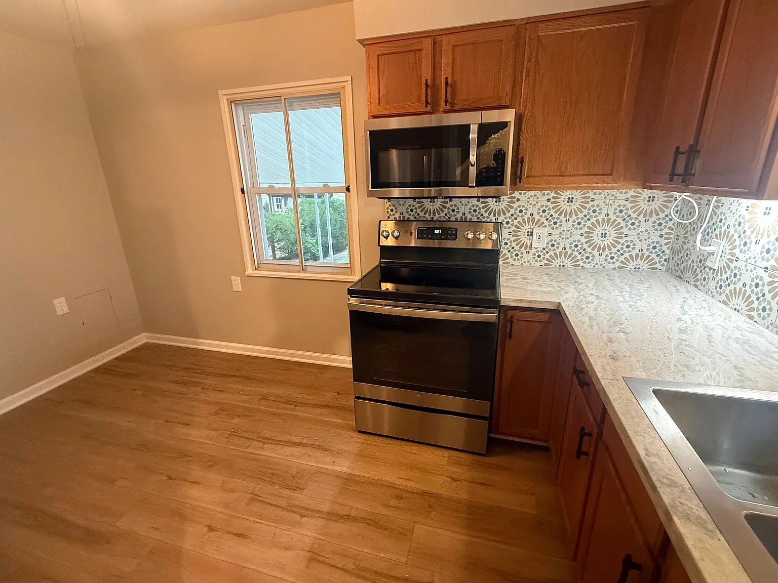 Updated kitchen with wood cabinets, stainless-steel range and microwave, and patterned tile backsplash